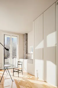 A modern home office featuring wooden flooring and a glass table with a black lamp and a wooden chair.