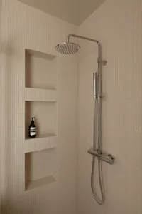 A modern minimalist shower with textured beige tiles, featuring a fixed showerhead and a handheld showerhead mounted on a chr