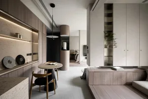 A minimalist living room with wooden furniture, open shelving, and a small dining area.