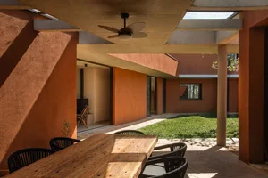 A modern porch with wooden table, concrete floor, and a view of a green lawn and house interior.