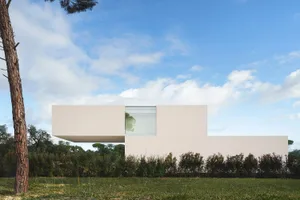 A minimalist, modern residential home with a concrete facade, surrounded by greenery and clear blue sky.