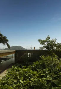 People standing on a modern veranda overlooking lush greenery and distant mountains under a clear blue sky.