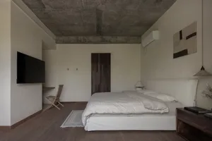 A modern industrial-style bedroom with concrete elements, featuring a single bed with white bedding and a minimalist design.