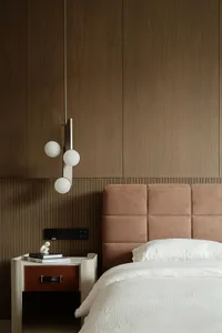 A minimalist bedroom featuring a textured wood wall and headboard, with a white bedspread and a modern light fixture.