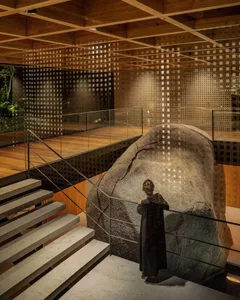 A person standing next to a large, textured rock in a modern indoor space with wooden floors and brick walls.
