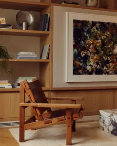 A modern living room featuring a wooden armchair, abstract art, and a bookshelf with books and decorative items.