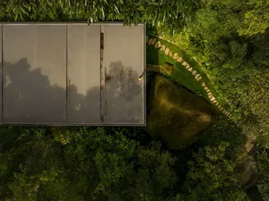 Aerial view of a modern landscape featuring a metal-roofed structure surrounded by lush greenery and a large rock formation.
