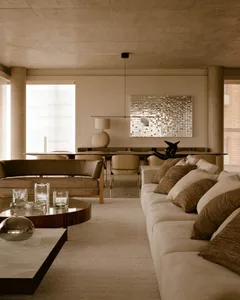 A modern living room with concrete walls and soft furnishings, including a long upholstered sofa with pillows and a round gla