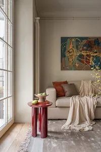 A modern living room featuring a contemporary art piece on the wall, a beige couch with cushions, and a red cylindrical table