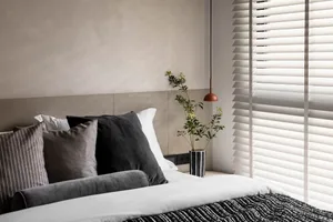 A neatly made bed with a modern minimalist design, featuring a wooden headboard, white bedding, and a green plant in a vase o