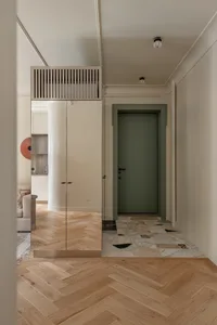 A modern minimalist hallway with wooden herringbone flooring and a green door.