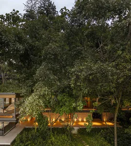 A modern residential house with wooden exterior and concrete accents surrounded by lush greenery.