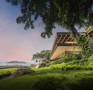 Modern style residential house made of wood with a sloping roof, surrounded by greenery and trees.