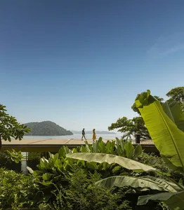 A modern vacation home featuring glass walls, a wooden patio, and a panoramic ocean view.