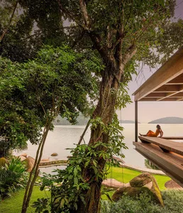 A person in an orange dress sitting on a wooden deck overlooking a serene lake surrounded by lush greenery and rocks.
