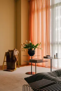 A cozy living room with a gray sofa, orange curtains, and white tulips in a vase on a glass table.
