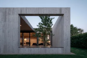 Concrete exterior of a minimalist home with a large triangular cut-out revealing a tree and interior space.