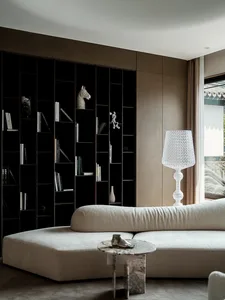 A minimalist living room with a white L-shaped sofa, a marble coffee table, and a white floor lamp. The background features b