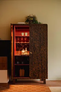 Modern bar cabinet with burl wood exterior and red interior, featuring glasses and bottles.
