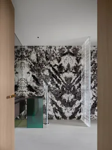 A modern bathroom with black and white marble walls, a green sink, and a glass divider.