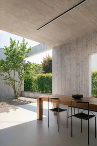 Modern, minimalist interior design featuring white flooring, concrete walls, and a wooden dining table.