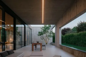 Contemporary living room with modern concrete walls and a glass wall overlooking an outdoor patio.