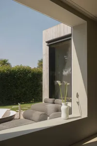 A modern lounge area with a large window that shows outdoor elements such as a hedge, a patio with a table and chairs, and a 