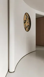 A modern decorative metal circle with geometric patterns on a white wall in a minimalist interior design setting.