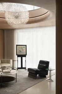 Luxurious modern living room interior with a round coffee table, black armchair, and a large crystal chandelier.