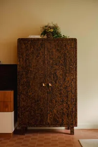 A modern living room with a wooden storage unit featuring two doors with gold handles, a vase of flowers on top, and a checke