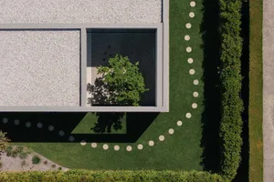 Modern public garden featuring a minimalist design with concrete pathways, green grass, and a central tree.