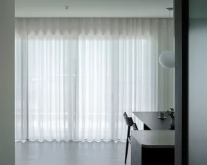 A minimalistic residential space featuring modern white curtains and matte black furniture.