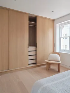 A minimalist bedroom featuring wooden cabinets with sliding doors and a white cushioned chair.