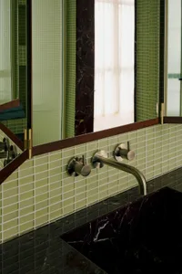 Green-tiled minimalist bathroom with marble accents, brass fixtures, and a large mirror.