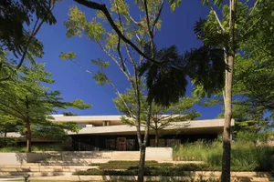 Modern minimalist residential house with concrete structure and surrounding greenery.