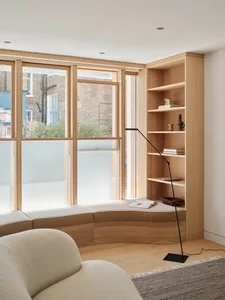 A minimalist interior design featuring a wooden shelf with a floor lamp, a beige plush armchair, and a rug.