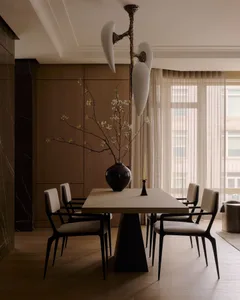 A modern dining room featuring wooden table, upholstered chairs, and metal pendant light.