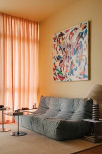 A modern living room featuring a colorful abstract painting on the wall, a plush fabric sofa, and a transparent side table wi