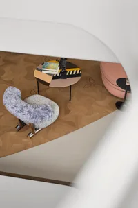 A modern living room with a wood floor pattern, featuring a colorful table with books and a statue, a circular sofa, and a pl