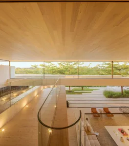 A modern living room with wooden floors, glass walls, and large windows overlooking greenery.