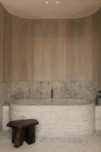 A minimalist bathroom featuring a marble bathtub and wooden accents.