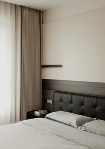 A minimalist bedroom featuring fabric curtains and a leather headboard with a side table and books.