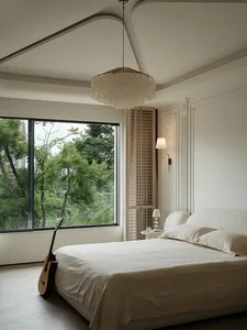 A minimalist bedroom featuring a white bed frame, ambient lighting, and a large window overlooking greenery.