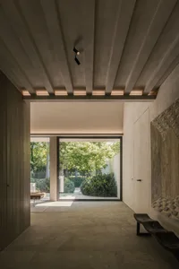 Interior design of a minimalist living room with concrete flooring and walls, featuring a large window with greenery outside.
