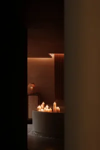 A modern bathroom featuring a concrete bathtub surrounded by candles and a wooden shelf.