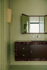 A modern bathroom featuring green mosaic tiles, a sink, and a cabinet.