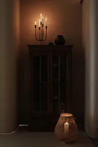 A dark wooden cabinet with a lit candlestick and a lantern on a dimly lit background.