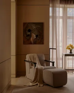 A cozy modern living room with a beige armchair, matching ottoman, and fabric drapes.