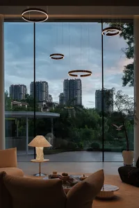 A modern living room with glass windows overlooking a cityscape at dusk, featuring a cozy seating area with a lamp and coffee