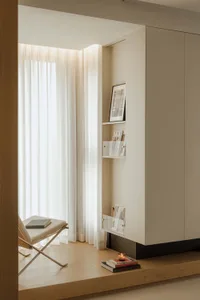 A minimalist residential interior featuring a white fabric chair, wooden surfaces, and metal accents.